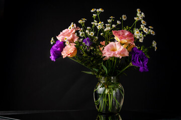 Bouquet of eustoma with boxwood and small-leaved branches on a table on a black background