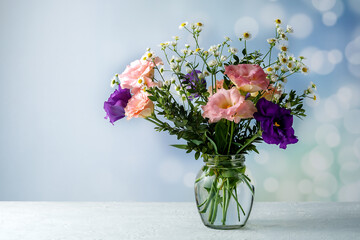 Bouquet of eustoma with boxwood and small-leaved branches on a table on a blue background