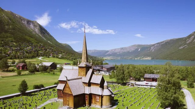 Wooden Church And Cemetery Under The Sunlight. Lom Stave Church With Otta River In Lom, Norway. aerial orbit
