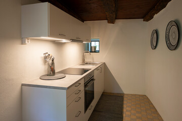 White kitchen in minimalist vacation apartment. The light under the wall units is on and illuminates the room