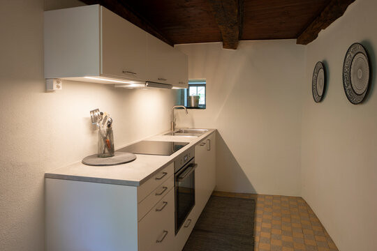 White kitchen in minimalist vacation apartment. The light under the wall units is on and illuminates the room