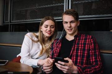 Positive young couple listening to music together in cafe