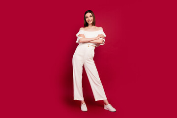 Full length photo of cool brown hairstyle millennial lady stand wear naked shoulders top pants isolated on red background