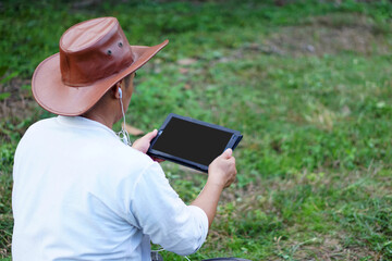 Concept : using   smart device everywhere in daily life. Handsome Asian gardener sit in garden and hold smart tablet to  study online and search knowledge about agriculture. 