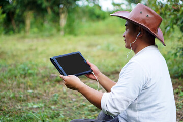 Concept : using   smart device everywhere in daily life. Handsome Asian gardener sit in garden and hold smart tablet to  study online and search knowledge about agriculture.  