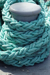 Close up of grey mooring bollard on the pier with blue naval rope on a sunny summer day. Marine....