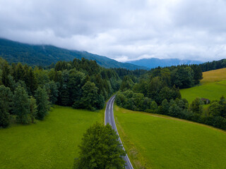 Aerial view of the road between green meadows fields in the countryside, village forest.