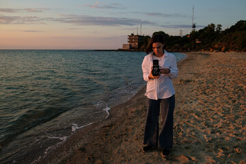 Fototapeta na wymiar Girl capturing sunrise over the sea on camera. Red dawn on the sea in the morning