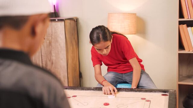 Shoulder shot of girl kid playing carrom board gamre by hitting red or queen coin after thinking - cocept of children playing indoor games