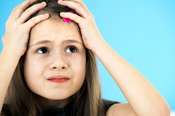 Close up portrait of upset and pensive little girl with cute pink hairpin on blue background.