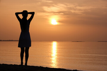Fototapeta premium Young woman relaxing alone on ocean sand shore by seaside enjoying warm tropical evening.