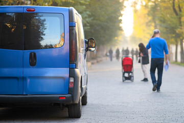 Passenger van car parked on a city alley street side with blurred walking pedestrians in autumn.