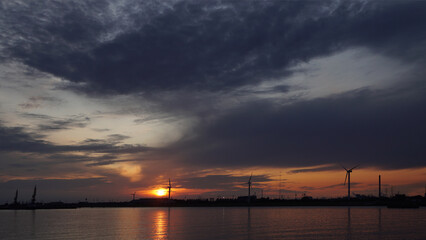 Fototapeta na wymiar silhouettes of wind turbines and cranes in the harbor at sunset, Hamburg, Germany