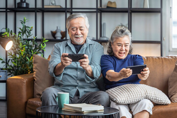 happiness asian retired couple enjoy playing and competition game smartphone mobile online together on sofa in living room home interior background,asian couple playing game together home isolate idea