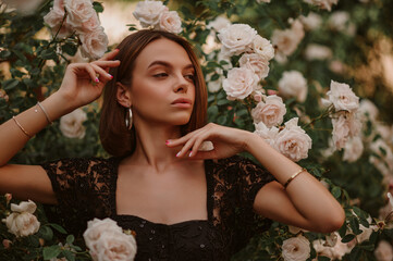 Summer street style, fashion portrait of beautiful brunette woman wearing stylish hoop earrings, black lace blouse, posing in street, near blooming roses. Copy, empty space for text  © Victoria Fox