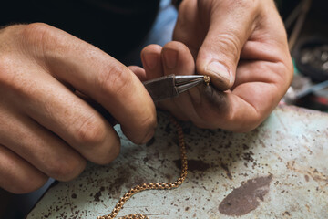 A jeweler repairs a gold chain, corrects the lock with pliers, close-up