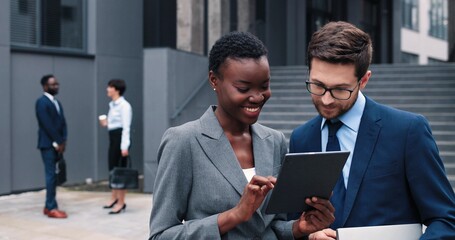 Glad to hear it. Portrait of optimistic young qualified manager is looking at his colleague female with smile while standing at the street and having pleasant communication