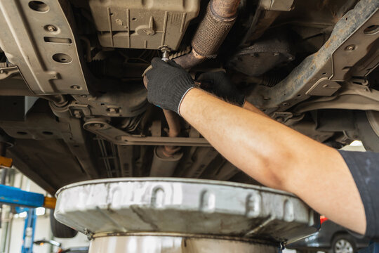 An auto mechanic tightens the oil drain plug in the crankcase of a car with a wrench