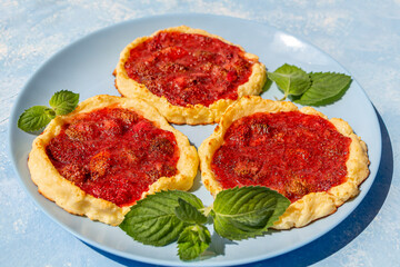 Homemade strawberry tartlet. Home сooking. Gluten free berries biscuit. Summer dessert on blue plate, decorated with mint leaf and icing sugar.