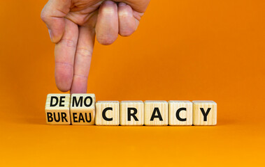 Democracy or bureaucracy symbol. Businessman turns wooden cubes and changes the word bureaucracy to democracy. Beautiful orange background, copy space. Business and democracy or bureaucracy concept.