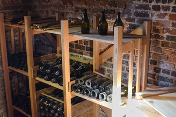 Old rustic bottles of wine in cellar wooden shelves against brick wall