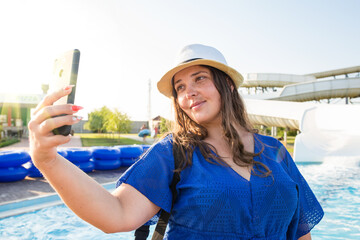 Young woman taking selfie in aquapark. Summertime vacation selfie. Girl taking picture in water park.