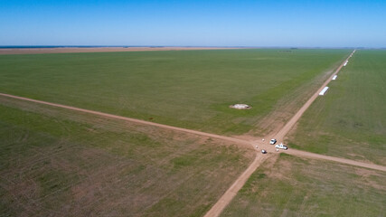 Aerial view of 4x4 pickup truck driving through wheat crops field with silos bags on the road. Argentina © claudio