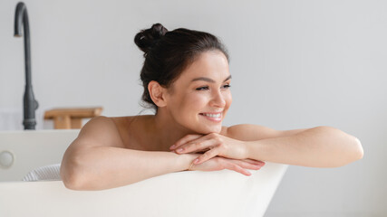Smiling serene peaceful young woman girl taking bath shower at home, relaxing in hot water after tedious day. Beauty treatment, body and skin spa care concept