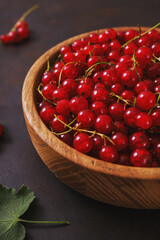 Fresh red currant in wooden bowl on dark table