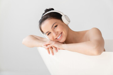Relaxing smiling serene young woman with brown hair resting in hot bath taking shower while...