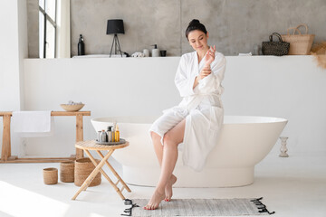 Young pretty woman using moisturizer hand body cream for taking care of her skin hands in spa bathrobe after shower bath. Beauty treatment concept