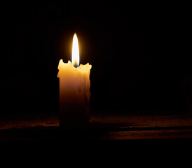 The flame of a burning candle in the dark. A single lit, melted candle on a black background. Close-up.