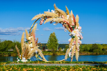 Fototapeta premium Wedding arch. A circular arch decorated with dried flowers and flowers on the shore of the pond.