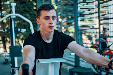 Portrait of an handsome young guy exercising on an outdoor sports simulator in the morning