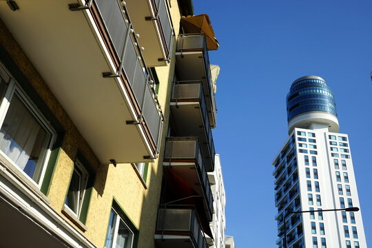 Gelbe Fassade eines Wohnhaus mit Balkons im Stil der Sechzigerjahre und moderne Architektur des neuen Henninger Turm vor blauem Himmel bei Sonnenschein am Hainer Weg in Frankfurt am Main Sachsenhausen