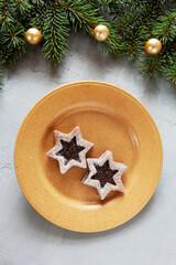 Christmas holiday background with fir-tree branches and balls, with homemade Linzer biscuits . Top view, close up, on light gray concrete background.