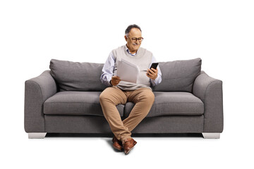 Mature man sitting on a sofa using a mobile phone and holding a paper document