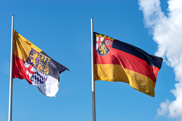 German flag on a flagpole waving in the wind with the coat of arms of the state of Rhineland-Pfalz and the town of Loreley.