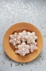   Homemade Christmas snowflake shape gingerbread on the dish.Top view, close up, on light gray concrete background with golden glitter confetti