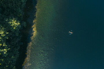 Summer landscape of a forest lake. A man swims alone and enjoys a warm day