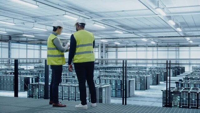 Korean Data Center System Administrators and African American IT Specialists in High Visibility Vests Talk, Use Laptop. IT Engineers work on Cyber Security Network Protection in Server Farm.