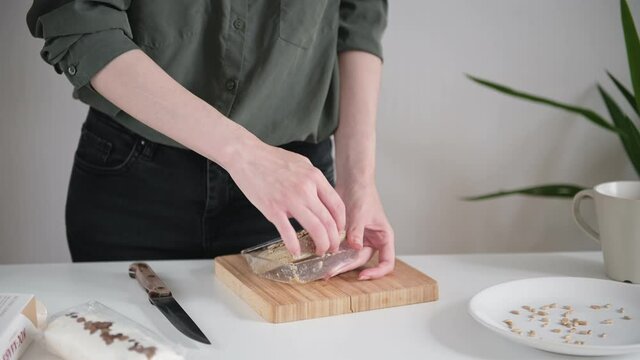 Lady in dark shirt takes delicious brown halva from transparent container and cuts into slices on board with knife close view.
