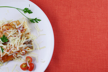 Pancakes with meat, in tomato sauce and cheese, with cilantro and grated cheese on top, and some cherry tomatoes on the plate.