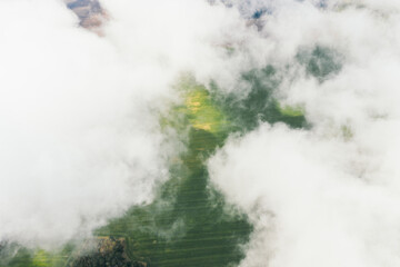 Aerial view of green farmland fields through white clouds. Shadows on the ground