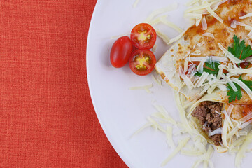 Pancakes with meat, in tomato sauce and cheese, with cilantro and grated cheese on top, and some cherry tomatoes on the plate.