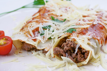 Pancakes with meat, in tomato sauce and cheese, with cilantro and grated cheese on top, and some cherry tomatoes on the plate.
