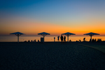 A beach with beach umbrellas and people on a summer evening at sunset