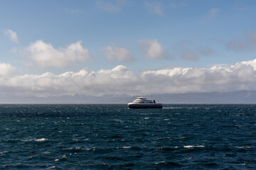 open ocean with whitecaps and a passenger ferry with the Lofoten Islands of Norway in the background
