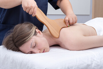 Fototapeta na wymiar Female hands are massaging the patient's back with a wooden massager, close-up. Woman having spa massage
