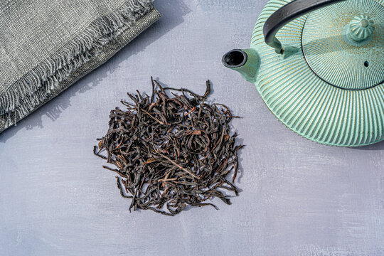 Dried Organic Black Tea Leaves on gray Background. Composition with Iron teapot and linen cloth. Asian tradition tea ceremony. High quality photo
